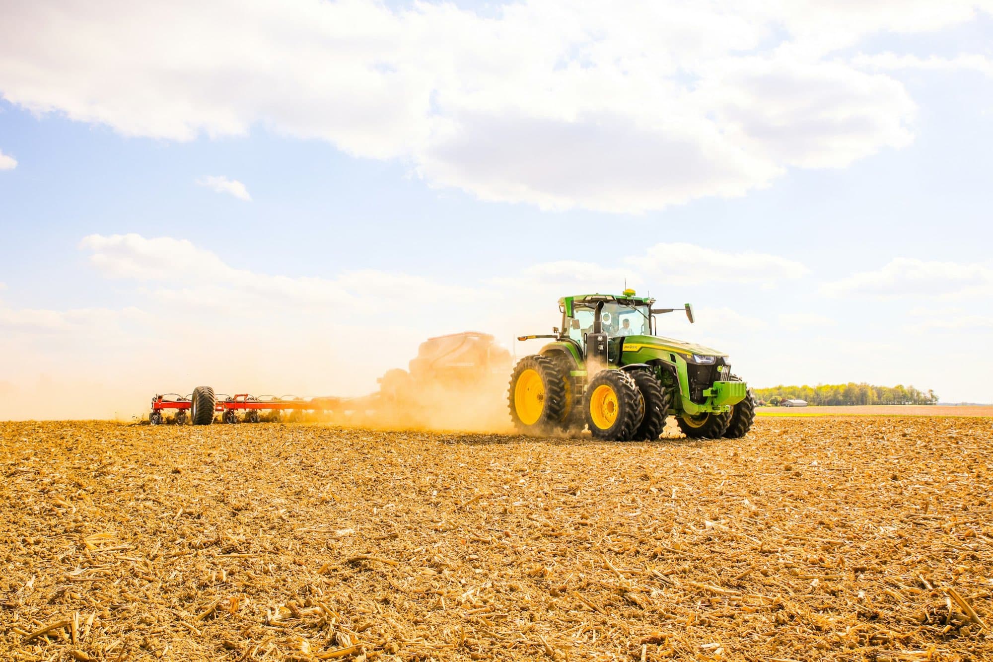 Row-crop tractor pulling an air seeder and planter bar across a tilled field in spring