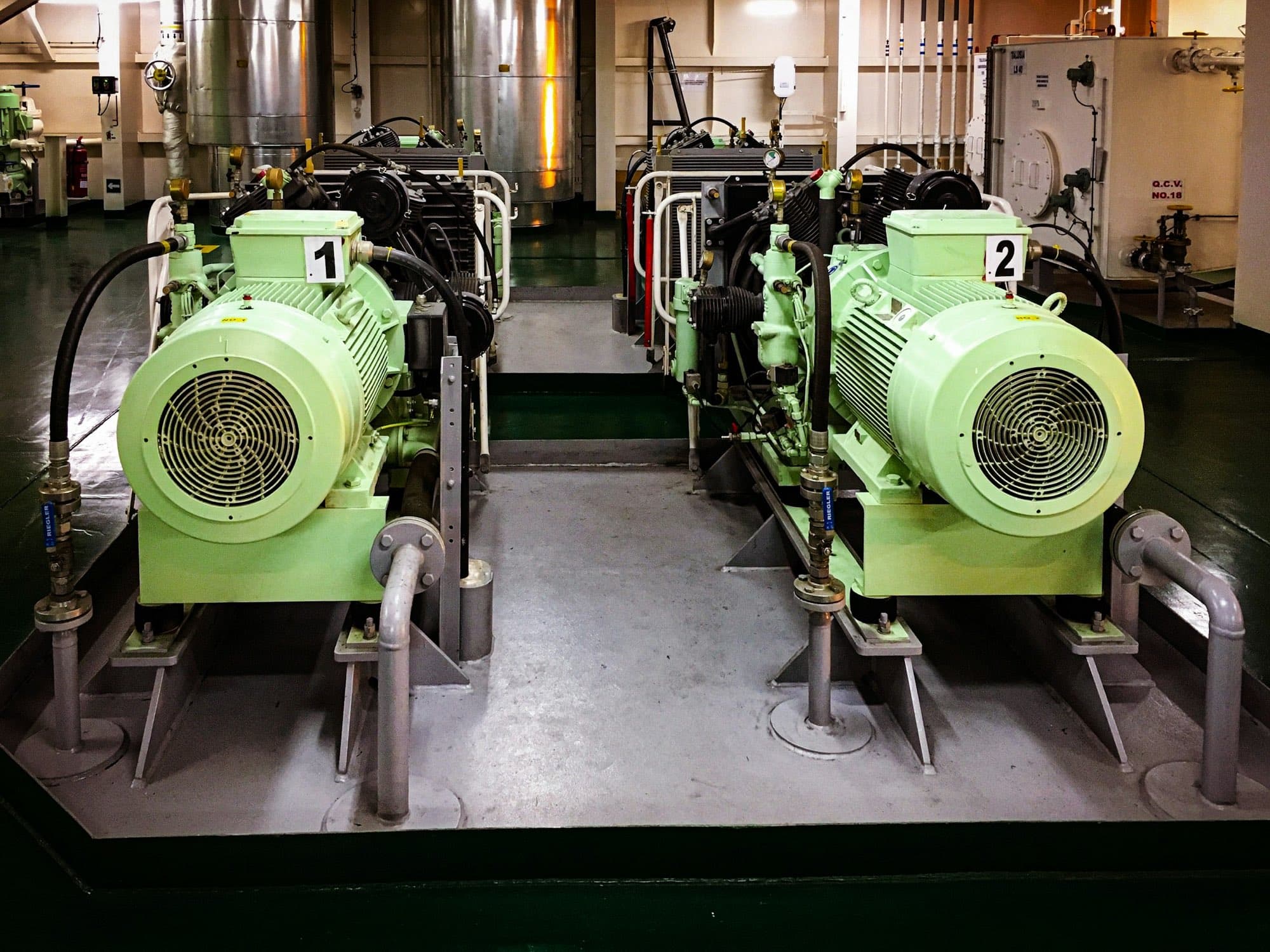 Two motor-driven reciprocating air compressors on steel skids with hoses, gauges and valves in a plant room