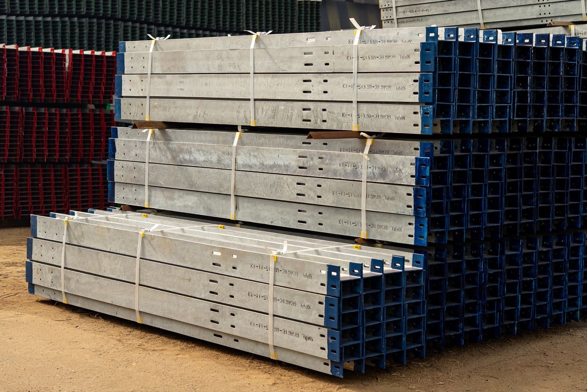 Strapped bundles of galvanized steel beams with punched holes stacked in a building materials yard