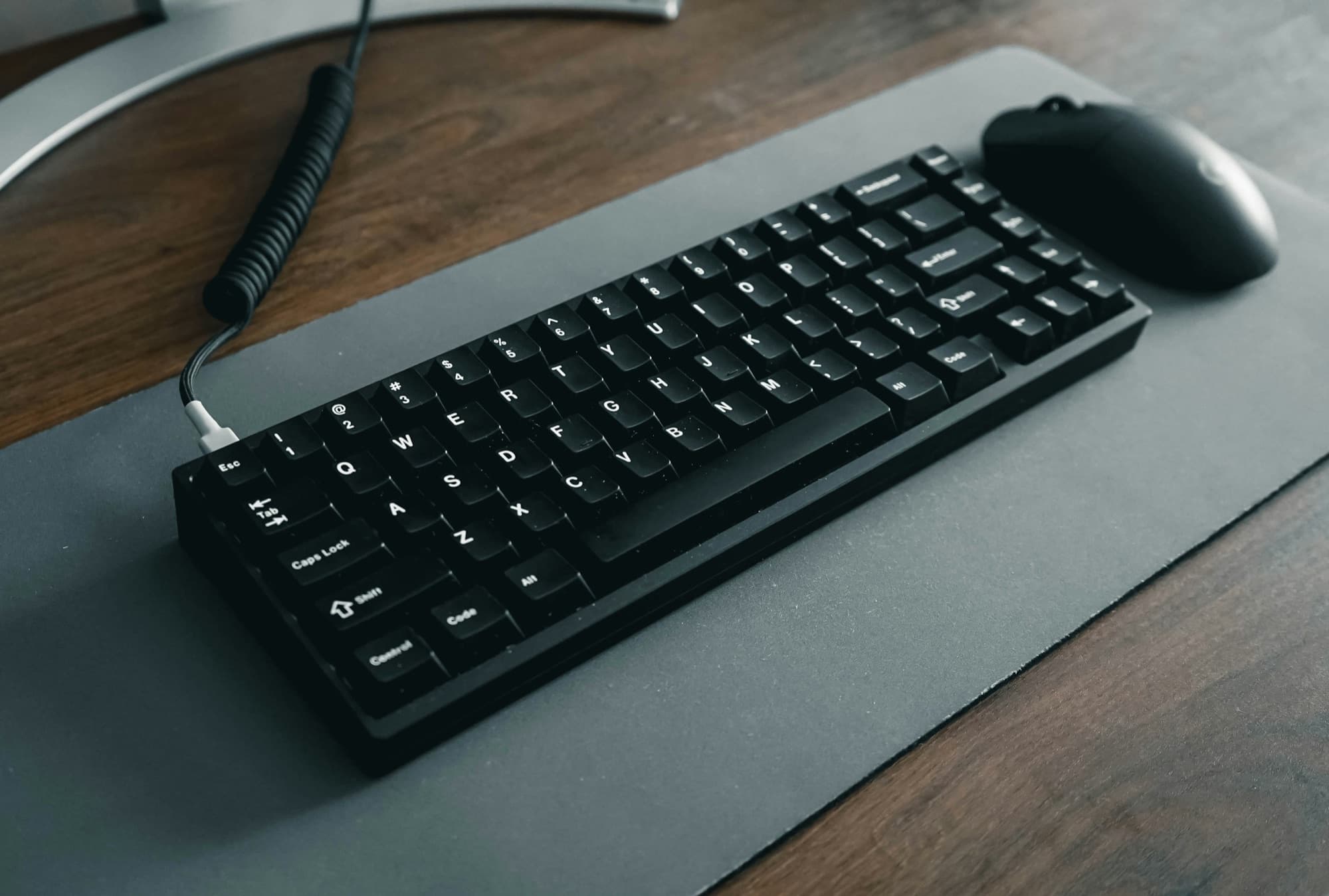 Compact mechanical keyboard with coiled USB-C cable and wireless mouse on a desk mat
