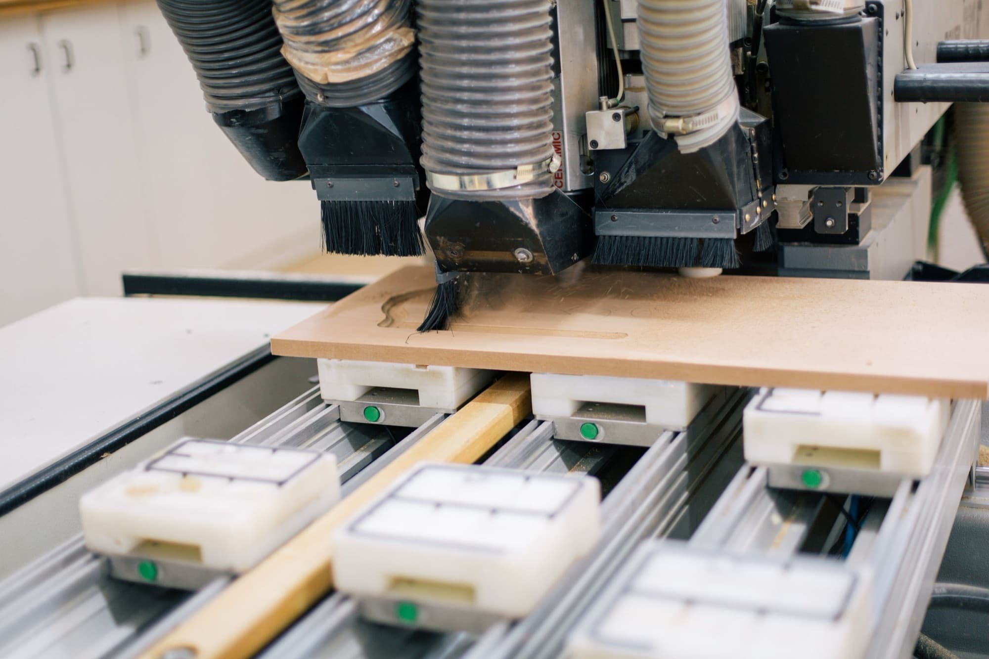 CNC router with dust hoods machining an MDF furniture panel held on vacuum pods
