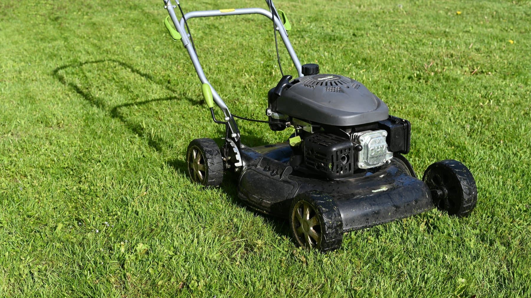 Gas-powered push lawn mower with steel deck, engine shroud and molded wheels on a freshly cut lawn
