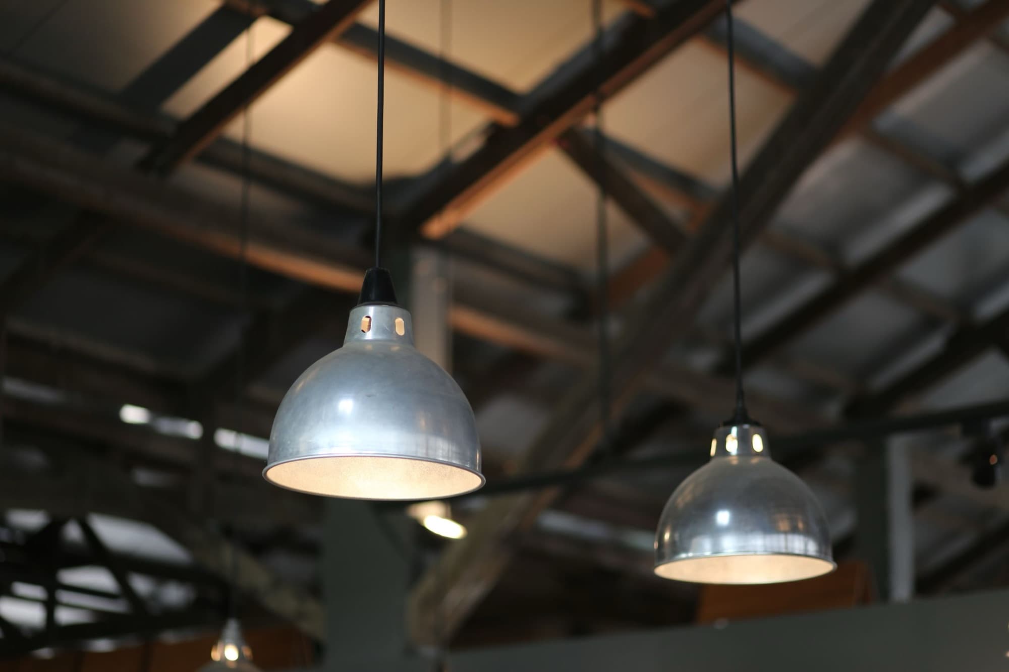 Spun aluminum industrial pendant light fixtures hanging from a warehouse roof structure