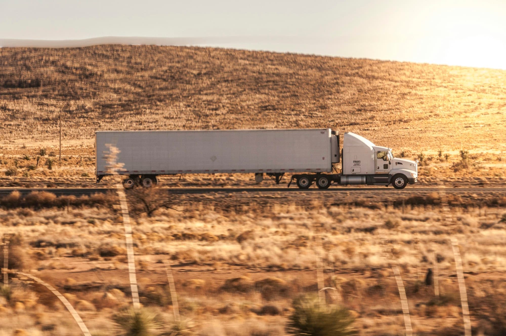 Semi truck hauling a refrigerated trailer along a desert highway at golden hour