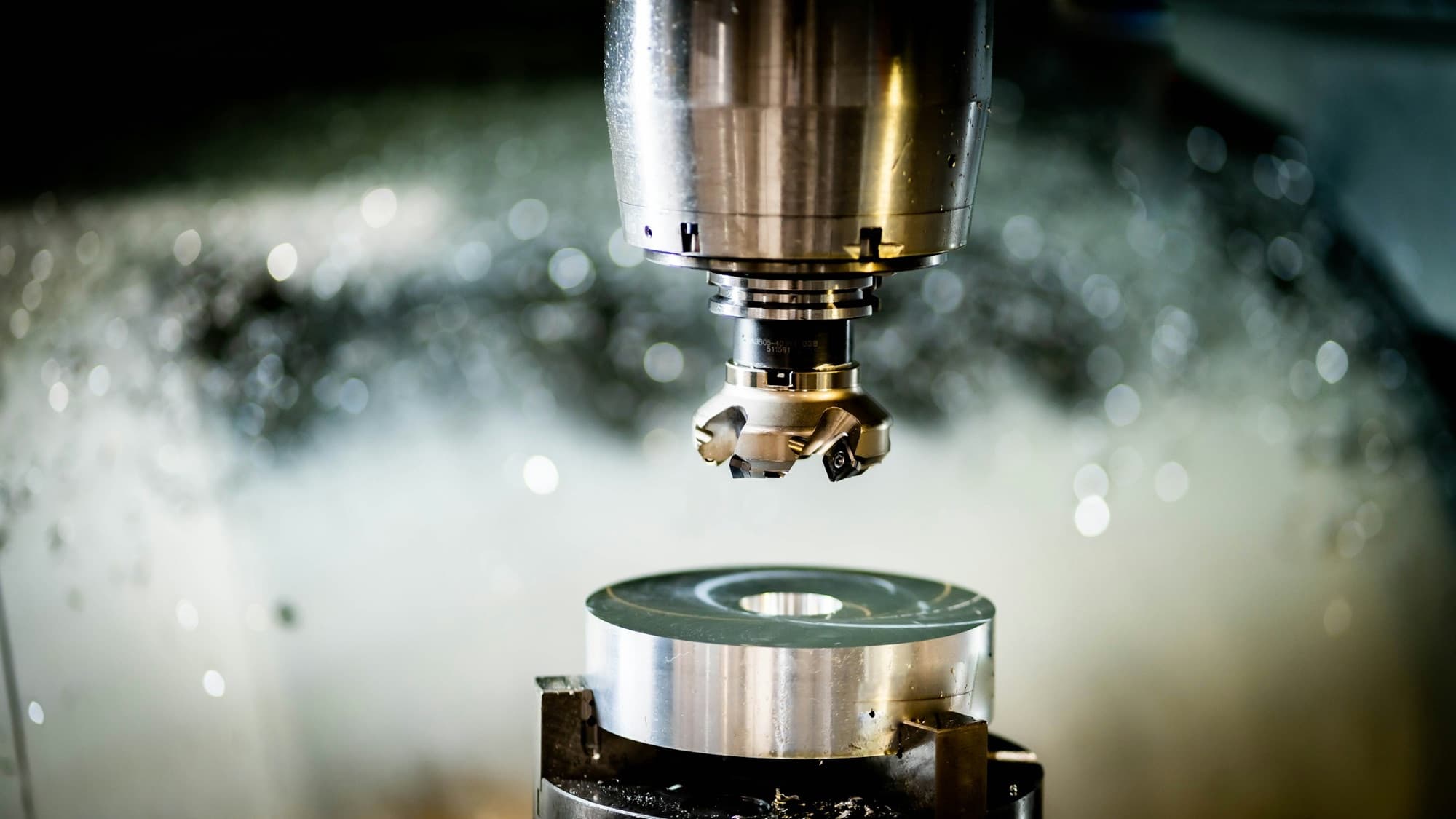 Indexable face mill above a round aluminum blank clamped in a vise inside a CNC mill