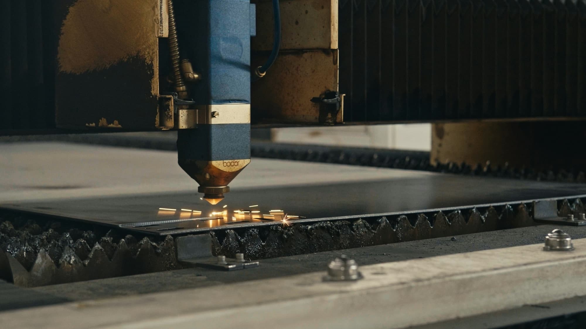 Fiber laser cutting head piercing a steel sheet on a slat bed, sparks along the kerf