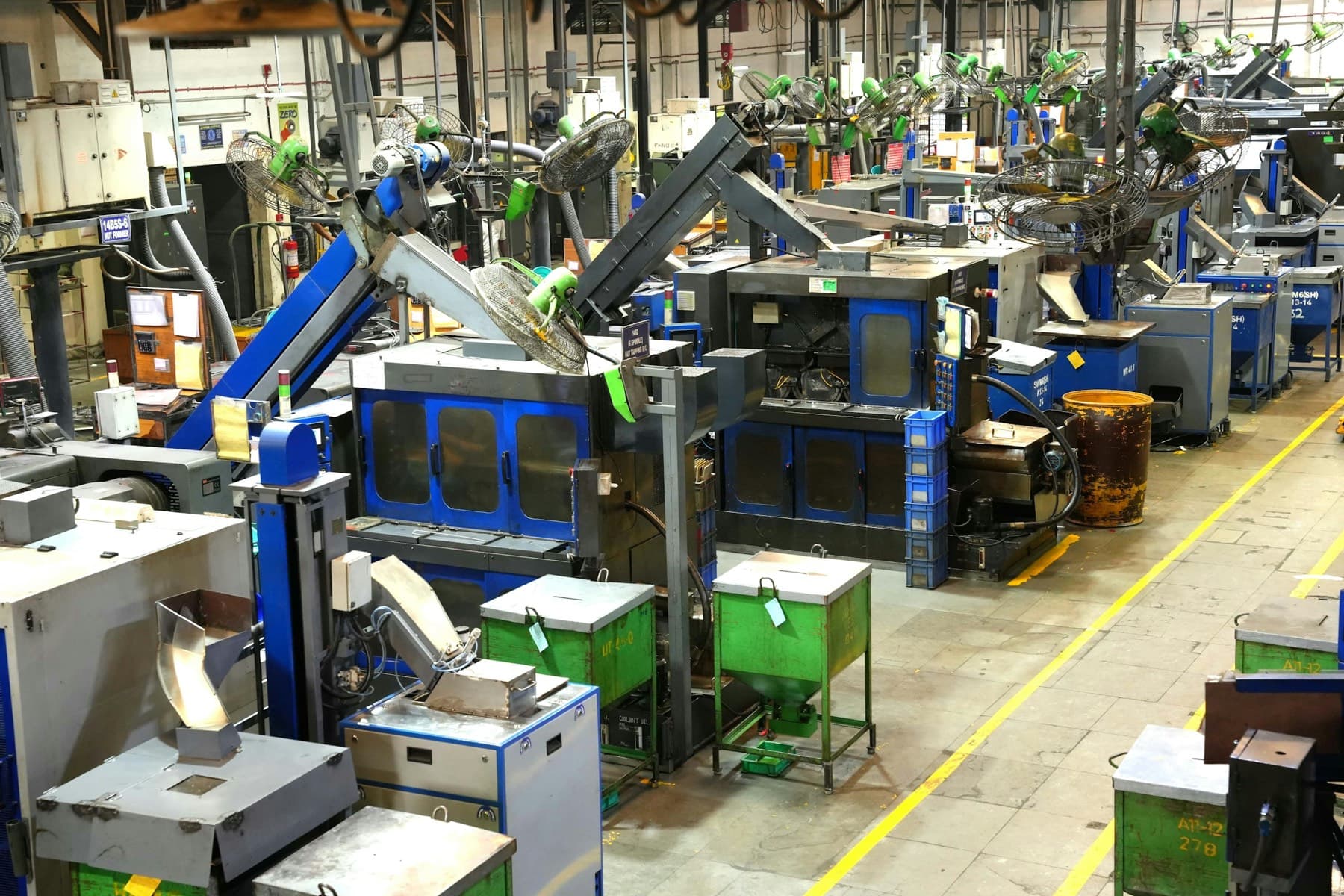 Rows of automatic nut formers and tapping machines feeding parts bins on a high-volume production floor