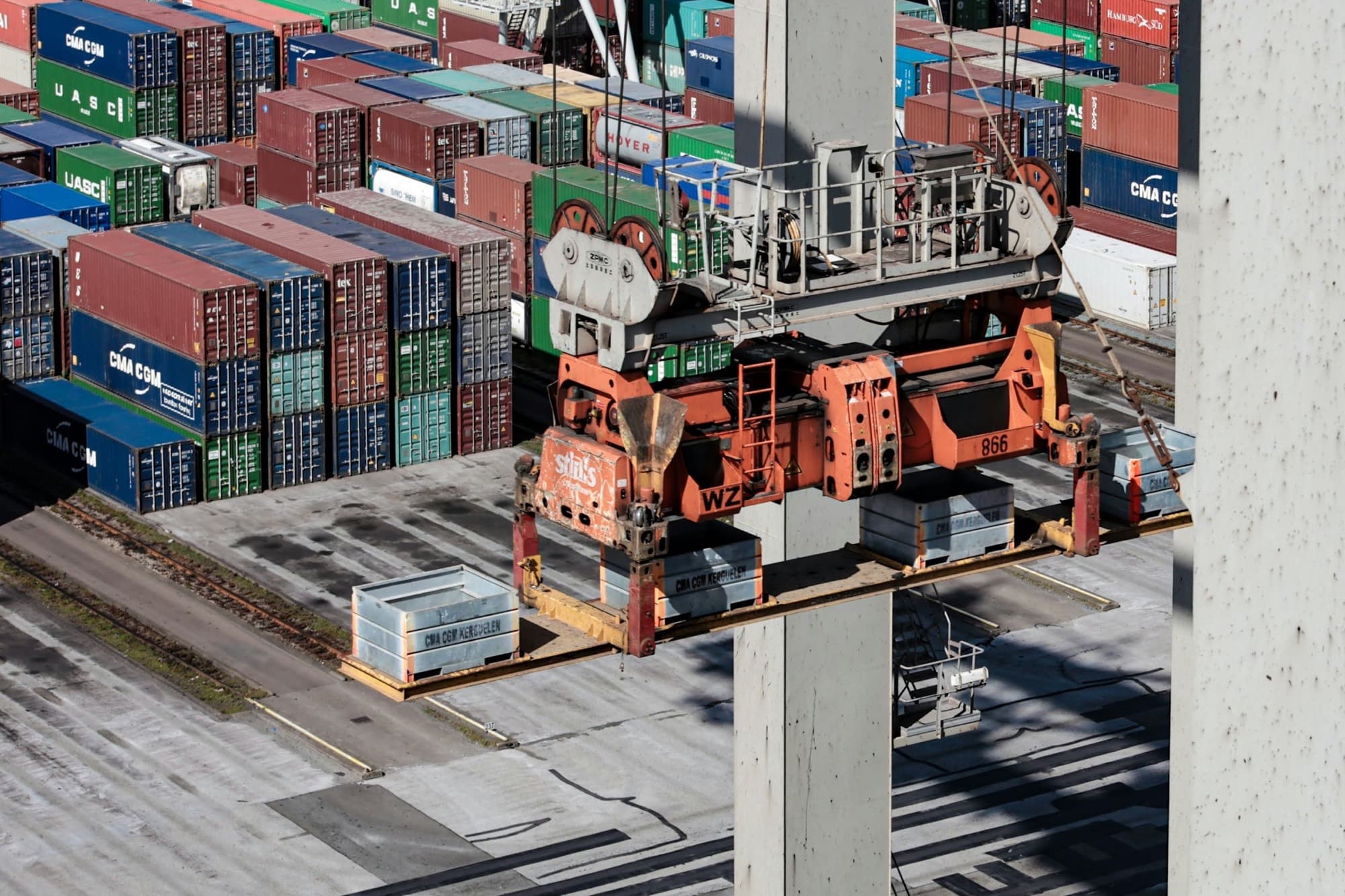 Ship-to-shore crane spreader lowering flat racks past stacked shipping containers at a container terminal