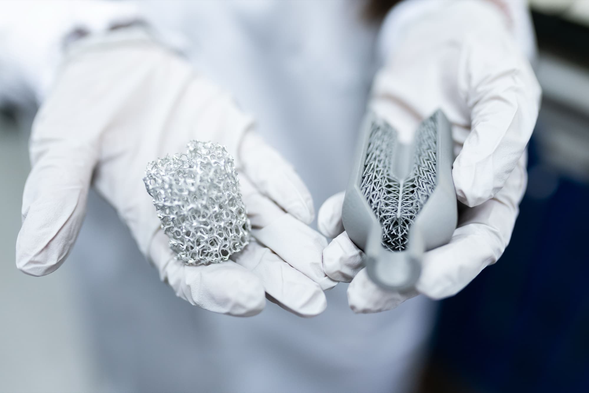 Gloved hands holding a metal lattice block and a 3D printed part with lattice infill inside a thin shell