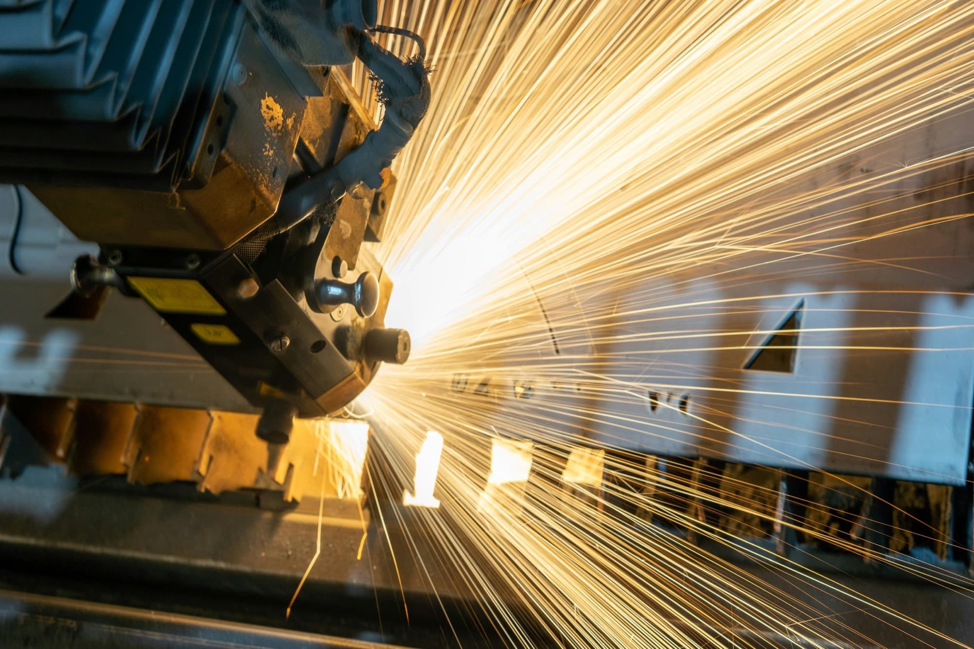 Laser cutting head slicing sheet steel on a slatted bed, throwing a fan of sparks