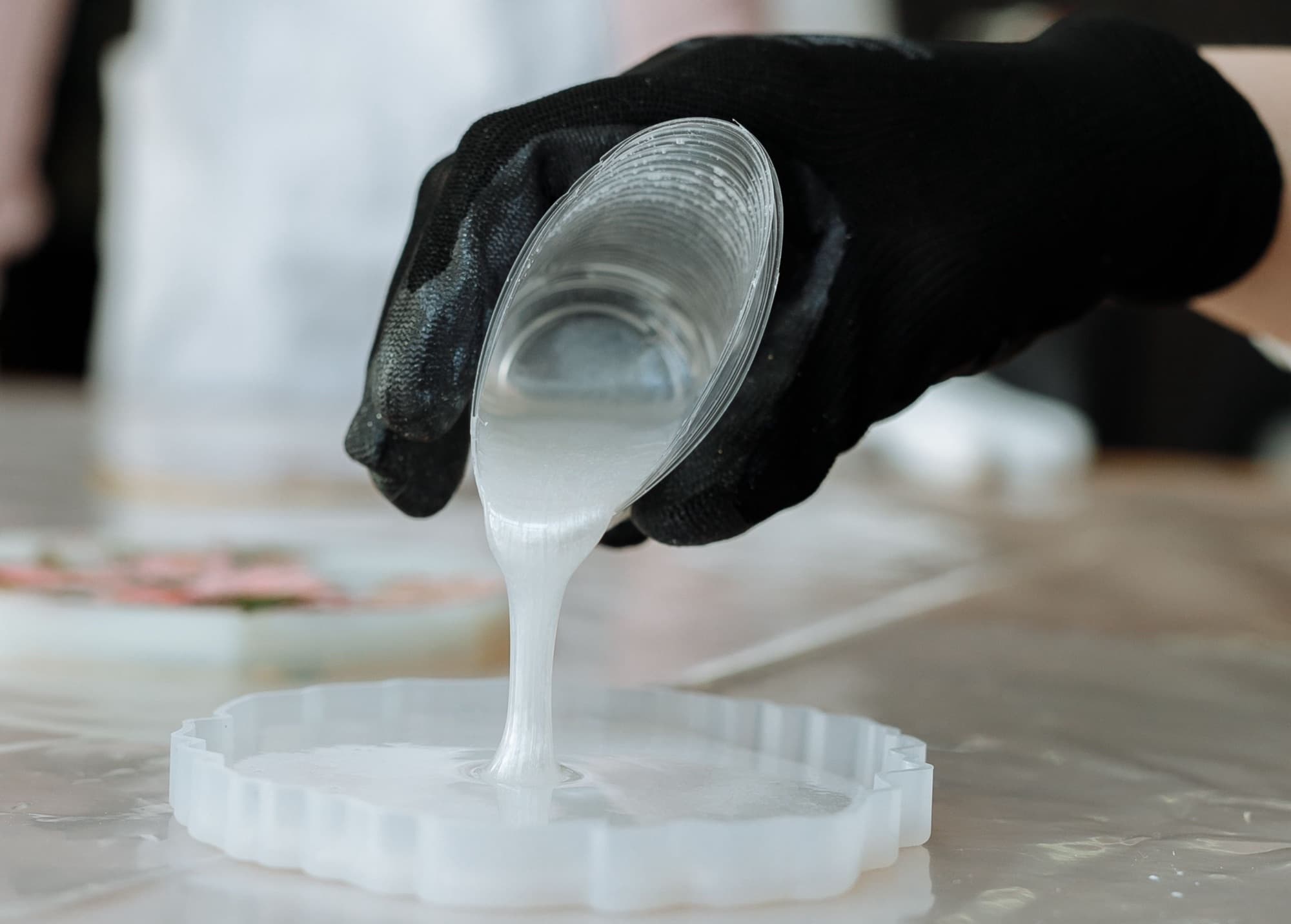 Gloved hand pouring mixed liquid resin from a cup into a flexible silicone mold