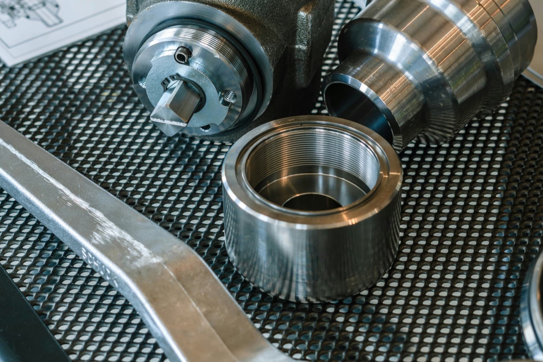 Turned steel sleeves and a cast valve body with machined bores laid out on a perforated inspection table