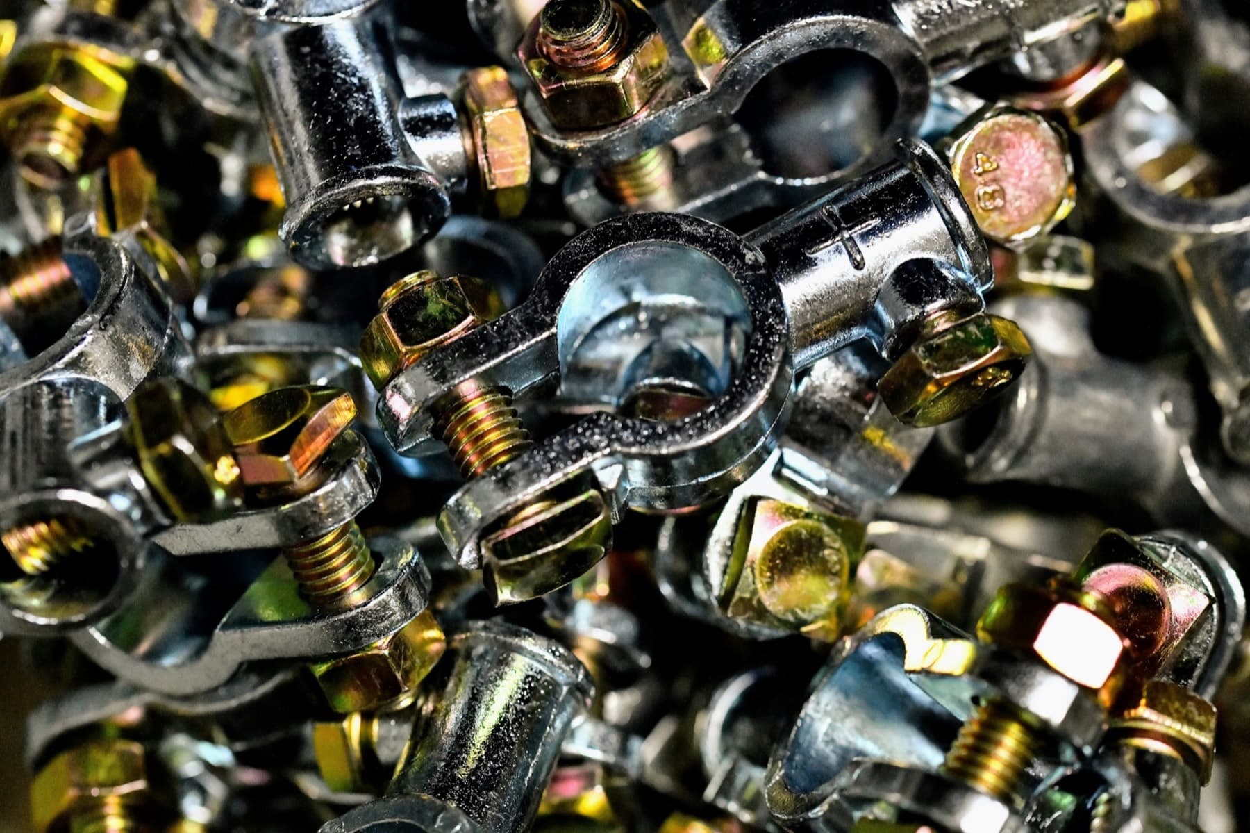 Heap of plated battery terminal clamps with hex bolts, a typical high-volume production part