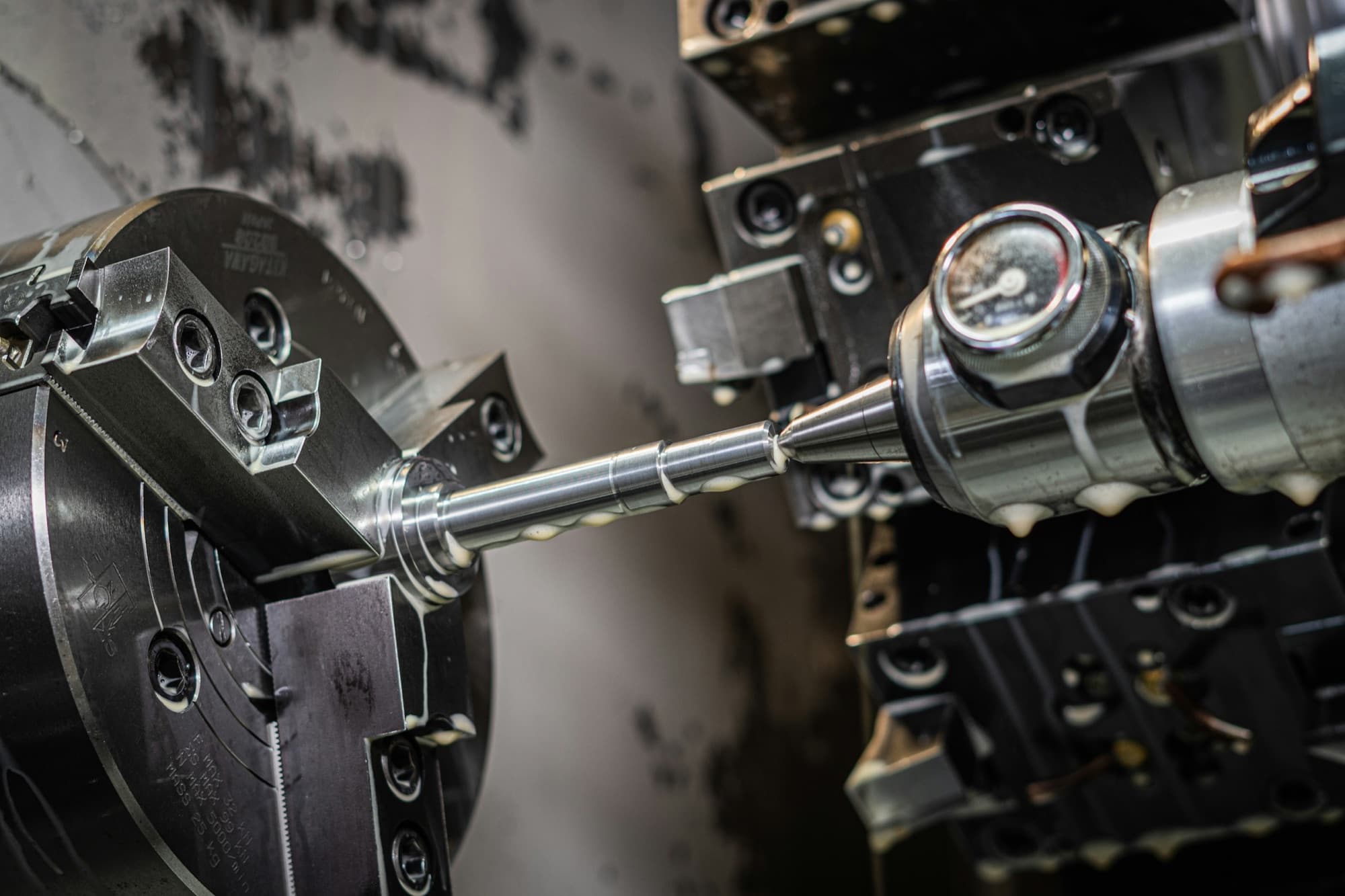 Stepped steel shaft held in a three-jaw chuck and supported by a live center on a CNC lathe