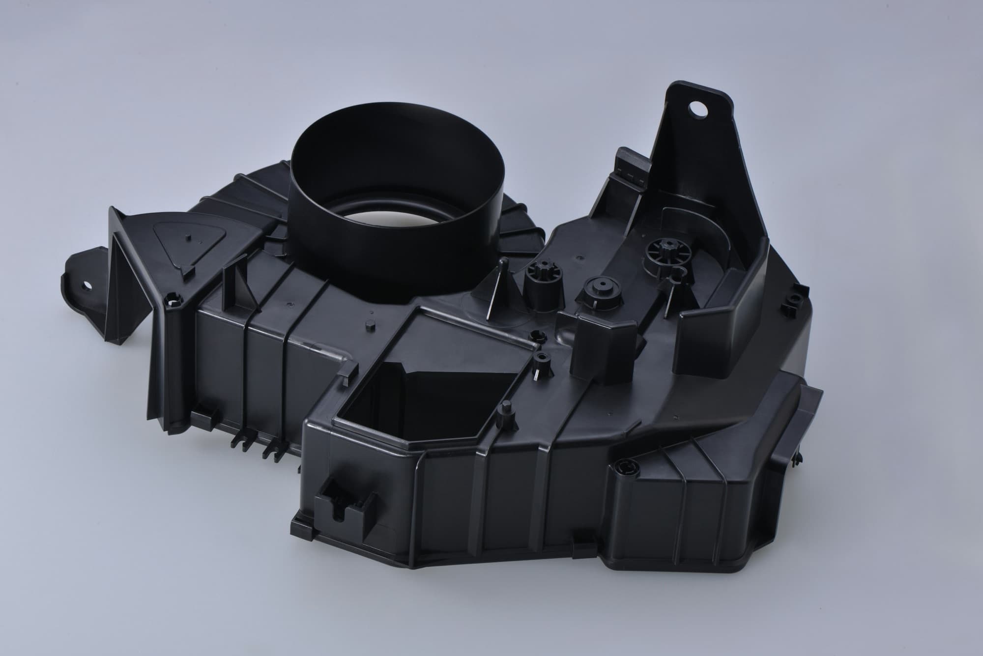 Black injection-molded production housing with ribs, bosses, snap fits and a round duct outlet