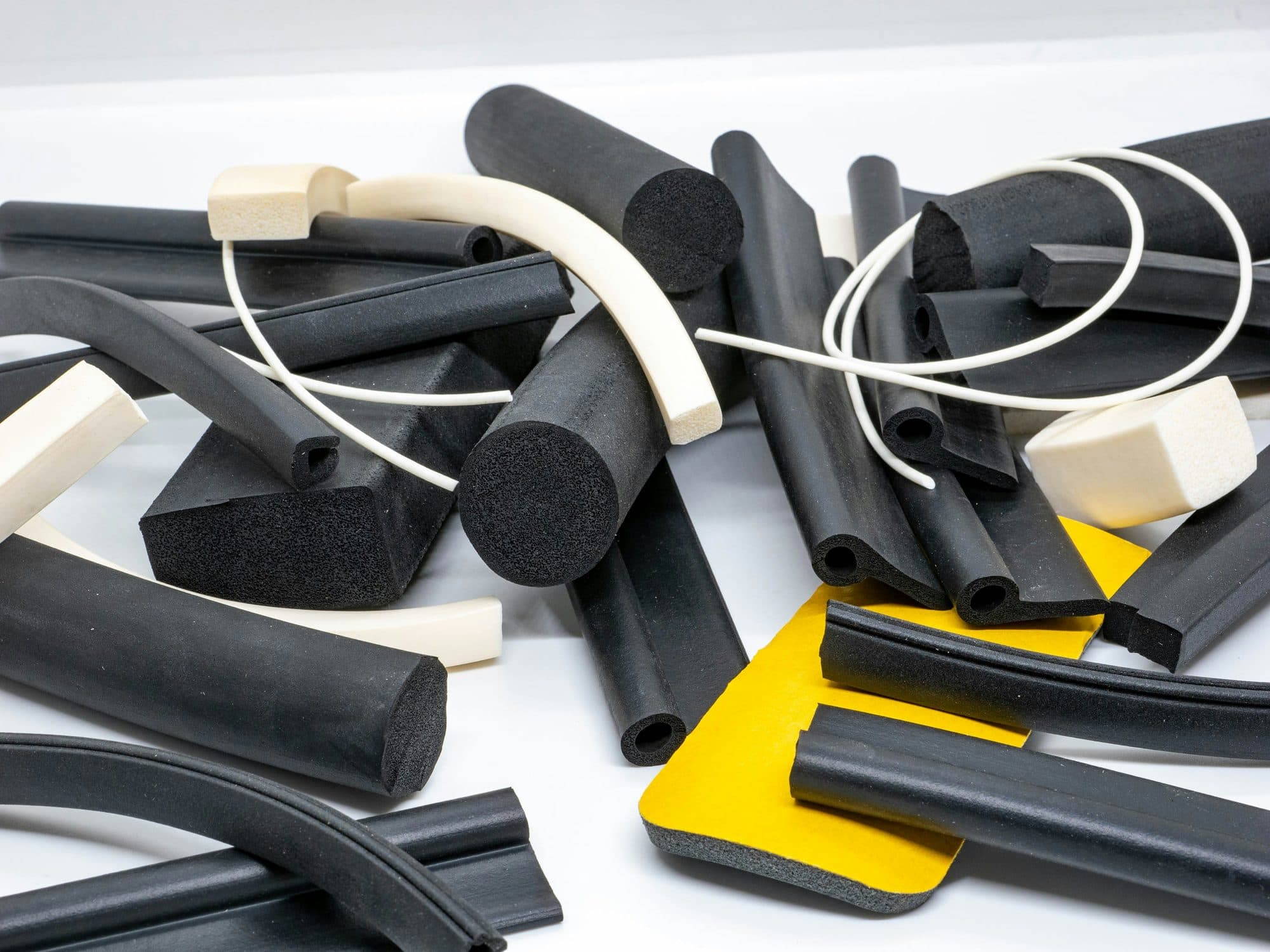 Cut lengths of extruded black rubber and white silicone sponge seal profiles showing their cross-sections