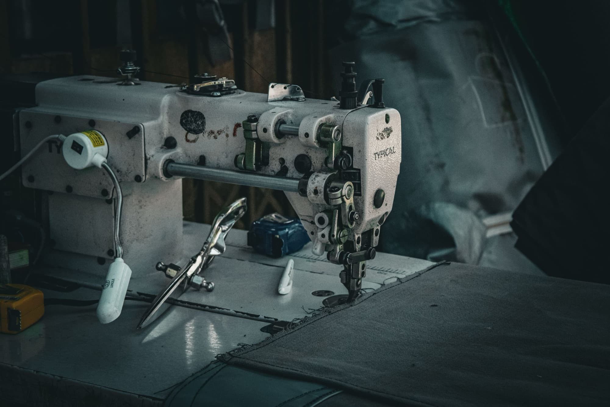 Industrial walking-foot sewing machine stitching heavy canvas, with shears and marker on the table