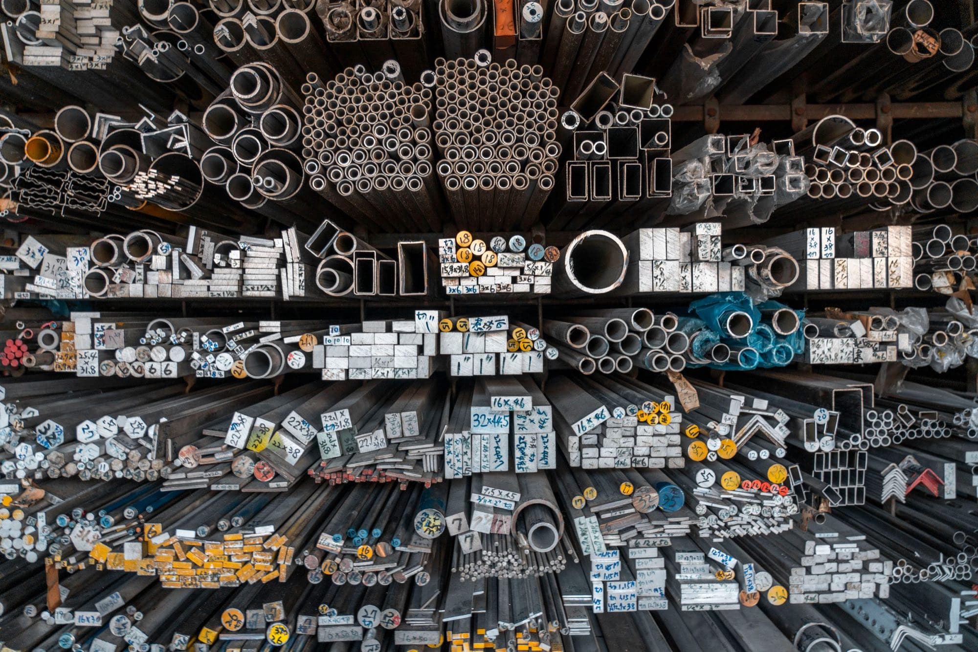 Racks of metal bar stock, tube and profiles with hand-marked sizes on the cut ends